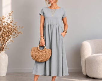 Peut inclure: Une robe midi gris clair à manches courtes, col rond et taille froncée. La robe présente une jupe ample et fluide avec des poches latérales. Elle est associée à un sac à main en paille tressée et des sandales à brides marron.