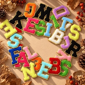 May include: A collection of colorful, fuzzy, varsity-style letter patches arranged in a circular pattern. The patches feature various letters of the alphabet in bright shades of orange, black, purple, green, blue, yellow, pink, white, and red.