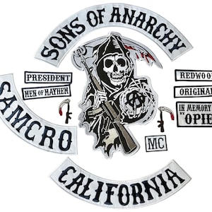 Pode incluir: Um conjunto de emblemas bordados com o logótipo Sons of Anarchy, incluindo uma figura central da morte com uma espingarda e uma foice, bandas curvas com os textos Sons of Anarchy, Samcro e California, e pequenos emblemas retangulares.