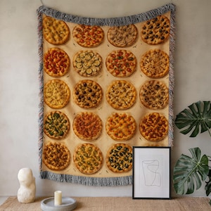 May include: A woven throw blanket featuring a repeating grid pattern of various round pizzas with different toppings. The blanket has a light beige background and is finished with a decorative fringe along the top and bottom edges.