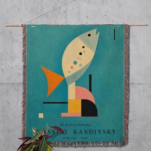 May include: A woven wall tapestry featuring a teal background with a stylized fish graphic in cream, orange, and black. The design includes geometric shapes and the text The Gallery Collection VASSILY KANDINSKY UPWARD 1929 at the bottom.