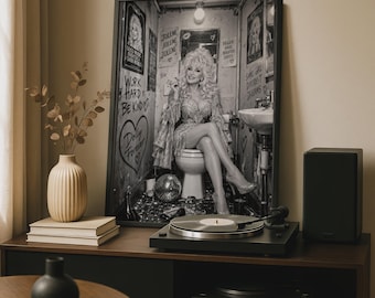 May include: A framed black and white wall art print featuring a portrait of Dolly Parton sitting on a toilet in a bathroom setting. The image includes text such as Work Hard Be Kind, Jolene, and Dolly Forever, alongside a disco ball on the floor.