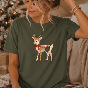 Op de afbeelding: Een militair groen t-shirt met korte mouwen en een afbeelding van een hert met gewei, versierd met een rode strik en een patchworkpatroon in rood, wit en beige. Het shirt wordt gecombineerd met een rood, wit en zwart geruite pyjamabroek.