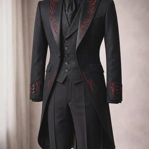 May include: A black tailcoat suit featuring a dark gray vest, a black shirt, and a black tie. The tailcoat is adorned with intricate red embroidery along the lapels and cuffs. The ensemble includes matching black trousers with a sharp center crease.