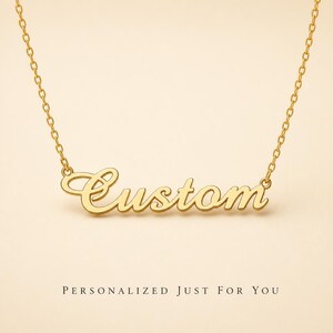 Puede incluir: Un collar de tono dorado con un colgante de placa con el nombre escrito en cursiva que dice la palabra Custom. El colgante está unido a una delicada cadena de tono dorado. Debajo del collar, el texto dice PERSONALIZED JUST FOR YOU.