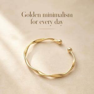 Puede incluir: Una pulsera abierta de tono dorado con una banda metálica ondulada y retorcida, con una pequeña cuenta esférica en cada extremo. El texto Golden minimalism for every day está impreso en letras marrón oscuro sobre la joya.