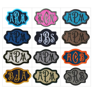 May include: A collection of twelve embroidered patches, each featuring a decorative scalloped border and a three-letter monogram in the center. The patches display various color combinations, including blue, pink, black, brown, gray, and orange.