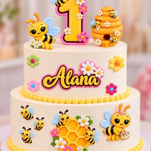 May include: A two-tier cake decorated with a bee theme, featuring the name Alana in pink and yellow script, a yellow number one, a beehive, honeycomb, and several cartoon bees with light blue wings, all accented with small colorful flowers.