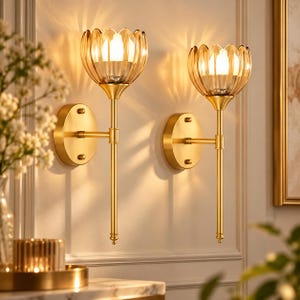 May include: A pair of wall sconces featuring a gold-toned metal finish with a slender vertical arm and a circular mounting plate. Each fixture is topped with a fluted, amber-tinted glass shade that houses a glowing light bulb.