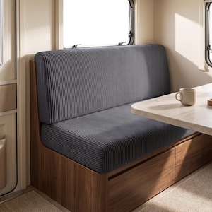 Puede incluir: Un banco de pana gris oscuro con respaldo alto, integrado en una base de madera con cajones de almacenamiento. El banco está situado junto a una mesa de color claro con una taza de cerámica y una pequeña bandeja de madera con servilletas.