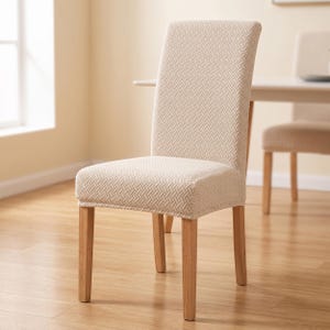 Puede incluir: Una silla de comedor con una funda de tela de color beige claro texturizada con un patrón de tejido de cesta. La silla tiene un respaldo alto y recto y cuatro patas de madera de tono claro, proporcionando una base estable para el asiento.