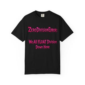May include: A black short-sleeved t-shirt featuring bright pink text that reads "ZERODIVISIONERROR: We All FLOAT Division Down Here" in a dripping, stylised font. The garment has a crew neckline and a standard fit, with a small white brand label.