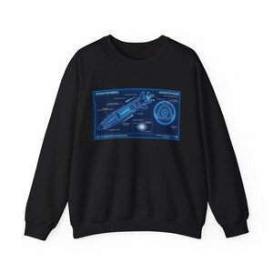 Puede incluir: Una sudadera negra de manga larga con un estampado gráfico azul de conceptos de armas de ciencia ficción. El diseño incluye diagramas técnicos de un misil y una bomba de antimateria con etiquetas, texto y flechas sobre un panel azul.