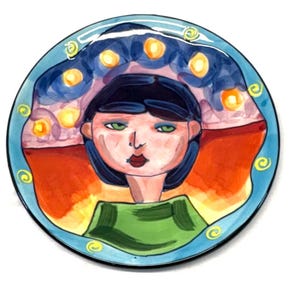 May include: A round ceramic plate featuring a hand-painted illustration of a person with dark hair, green eyes, and red lips. The figure wears a green top against a background of orange, purple, and yellow circular light motifs with a blue border.