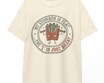 May include: A cream-colored short-sleeve t-shirt featuring a circular graphic of a cartoon french fry container lifting dumbbells. The text reads: MY STOMACH IS FLAT... THE 'L' IS JUST SILENT. The design uses muted red, green, and brown tones.