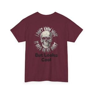 Peut inclure: Un t-shirt à manches courtes bordeaux avec un motif de crâne portant des lunettes. Le texte entourant le crâne indique I DON'T KNOW WHAT IT SAYS ON MY SHIRT, et sous le crâne, le texte But Looks Cool est écrit dans une police noire grasse.