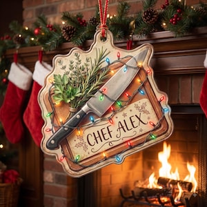 May include: A decorative hanging sign featuring a kitchen knife and a bundle of fresh herbs on a wooden cutting board background. The text CHEF ALEX is printed in black script. A string of colorful Christmas lights wraps around the board.