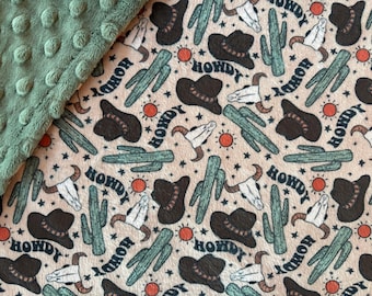 May include: A beige fabric with a repeating pattern of brown cowboy hats, green cacti, white skulls, and the word "Howdy" in a brown script font.