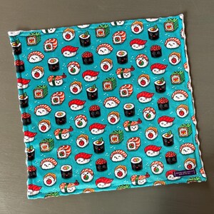 May include: Square, turquoise fabric with a repeating pattern of smiling sushi rolls. The sushi includes nigiri, maki, and other varieties, with red, white, and black accents. The fabric has a white border.