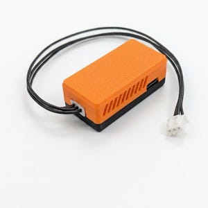 May include: A rectangular electronic component housing with a bright orange top section featuring diagonal ventilation slats and a solid black base. Two thin black wires extend from one side, terminating in a white plastic three-pin connector.