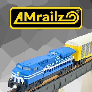 Könnte beinhalten: Eine blaue Spielzeugeisenbahn-Lokomotive mit dem Wort NORAM und einem F-Logo an der Seite, gekoppelt an einen gelben Güterwagen auf einer grauen Kunststoffschiene. Das AMrailz-Logo ist in einem gelb umrandeten schwarzen Rechteck zu sehen.