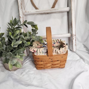 Peut inclure: Un panier rectangulaire en bois tressé avec une anse verticale unique. Le panier est doté d'une doublure en tissu amovible à bord volanté, ornée d'un motif floral coloré dans des tons de bleu, rouge et vert sur un fond crème.