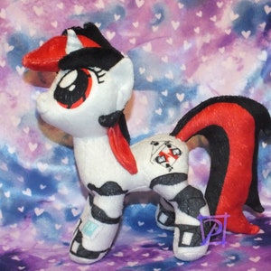 May include: A white and black plush unicorn with red accents. The unicorn has a black mane and tail, and a red horn. The unicorn has a black and white symbol on its flank.