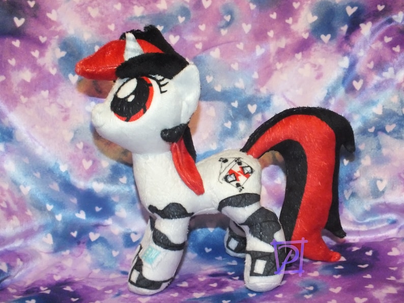 May include: A white and black plush unicorn with red accents. The unicorn has a black mane and tail, and a red horn. The unicorn has a black and white symbol on its flank.