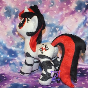 May include: A plush toy pony with a black and white striped body, red and black tail, and a red mane. The pony has a black and white striped horn and a red eye.