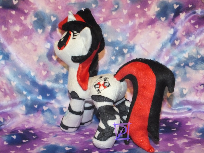 May include: A plush toy pony with a black and white striped body, red and black tail, and a red mane. The pony has a black and white striped horn and a red eye.