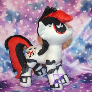May include: A black and white plush toy pony with red accents. The pony has a black mane and tail, and a red heart symbol on its flank. The pony is standing on a purple and blue background with white hearts.