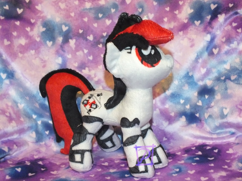 May include: A black and white plush toy pony with red accents. The pony has a black mane and tail, and a red heart symbol on its flank. The pony is standing on a purple and blue background with white hearts.