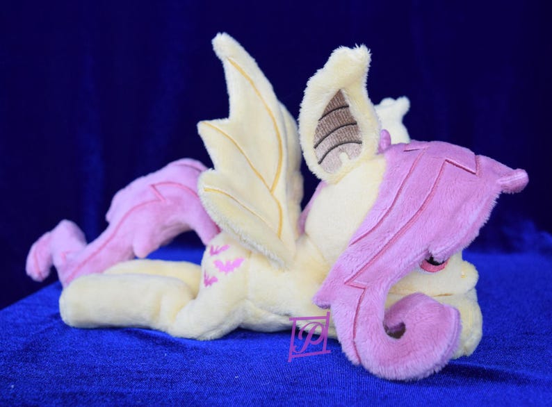 Pode incluir: Um brinquedo de pel&uacute;cia de um p&ocirc;nei alado rosa e amarelo com uma crina e cauda rosas. O p&ocirc;nei est&aacute; deitado de lado com a cabe&ccedil;a apoiada na sua perna da frente.