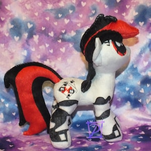 May include: A black and red plush toy pony with a white body and black and white markings. The pony has a red and black mane and tail, and a red bandana on its head. The pony has a black and white design on its flank that includes playing cards.