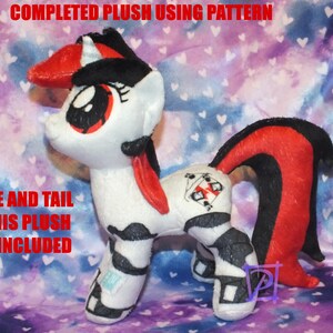May include: A white plush pony with black and red hair. The pony has a black and white pattern on its body and a red and black tail. The pony is standing on a purple and white background. The text "MANE AND TAIL OF THIS PLUSH NOT INCLUDED" is visible in the image.