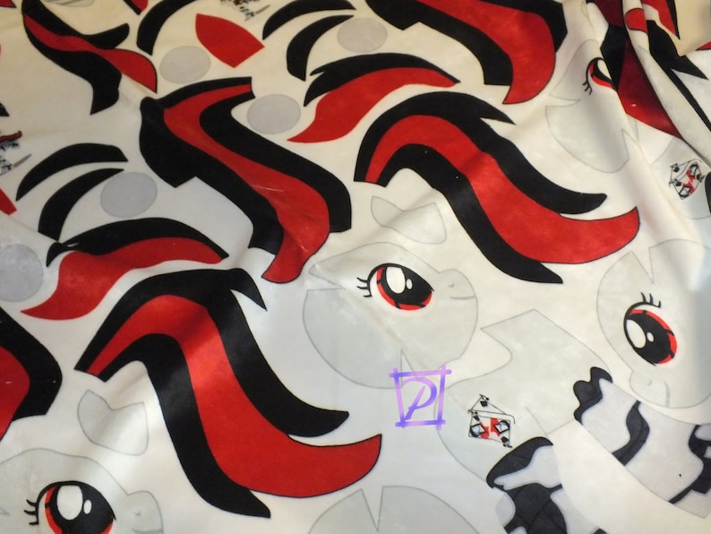 May include: White fabric with a repeating pattern of black and red stripes. The fabric features a cartoon pony face with a red eye and black eyelashes. The fabric is designed for sewing projects.