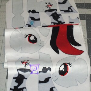 May include: White fabric with a pattern of a cartoon pony with a red eye and black mane. The fabric is cut into different shapes for sewing a plush toy.
