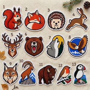 May include: A collection of thirteen embroidered patches featuring various animals including a squirrel, fox, hedgehog, rabbit, deer, bear, wolf, eagle, lynx, ibex, bison, robin, and puffin, each numbered from one to thirteen on a light fabric.