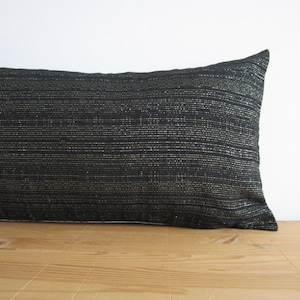 Puede incluir: Un cojín lumbar negro y dorado con tejido texturizado.