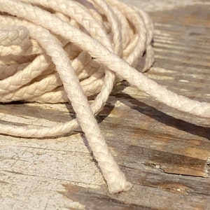 May include: A close-up of a white cotton cord, braided and twisted, lying on a weathered wooden surface.