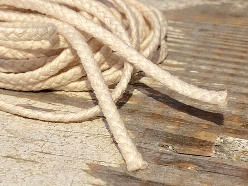 May include: A close-up of a white cotton cord, braided and twisted, lying on a weathered wooden surface.