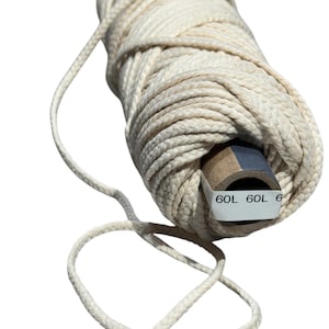 May include: A roll of natural white cotton twine with a brown cardboard core. The twine is wrapped around the core and has a loose end hanging off. The core has the text "60L 60L 6" printed on it.