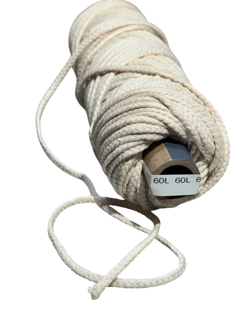 May include: A roll of natural white cotton twine with a brown cardboard core. The twine is wrapped around the core and has a loose end hanging off. The core has the text "60L 60L 6" printed on it.
