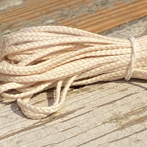 May include: A close-up of a white braided cotton cord, tied with a rubber band. The cord is on a wooden surface.