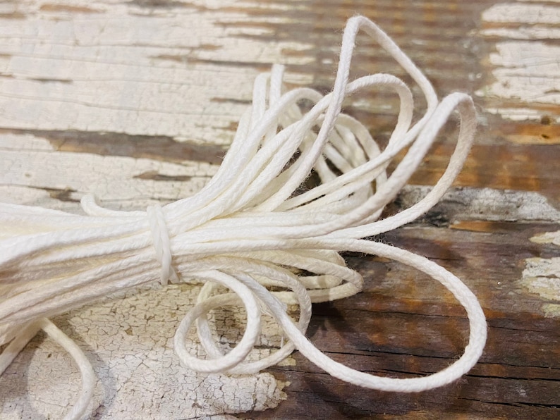 May include: A close-up of a white cotton cord, twisted and coiled on a wooden surface. The cord is soft and pliable, perfect for crafting or macrame projects.