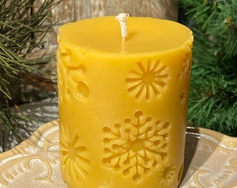May include: A yellow beeswax candle with a white wick and a decorative snowflake pattern. The candle is sitting on a white ceramic plate.