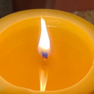 May include: A yellow candle with a single flame burning in the centre.
