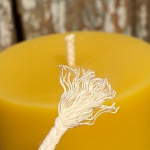 May include: Close-up of a white cotton candle wick, frayed at the end, against a yellow beeswax candle.