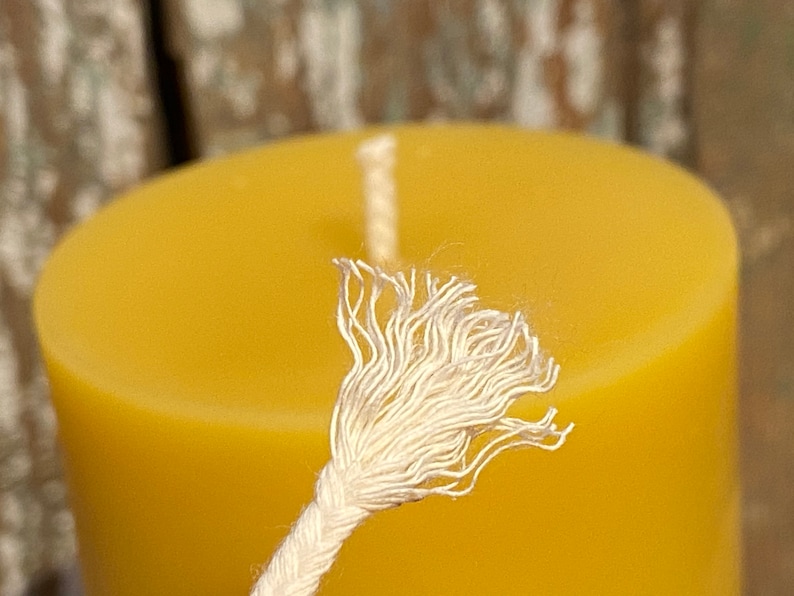 May include: Close-up of a white cotton candle wick, frayed at the end, against a yellow beeswax candle.