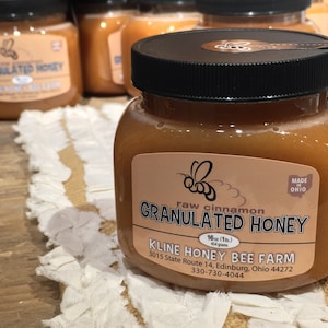 May include: A glass jar of raw cinnamon granulated honey, labeled "Kline Honey Bee Farm", with a bee logo and the text "Made in Ohio".